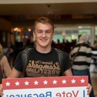 Student holding sign titled "I vote because: I want to make a difference"